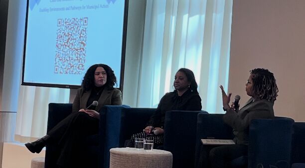 Three panelists seated on a stage in front of a presentation screen during a Columbia Climate School panel at NYC Climate Week